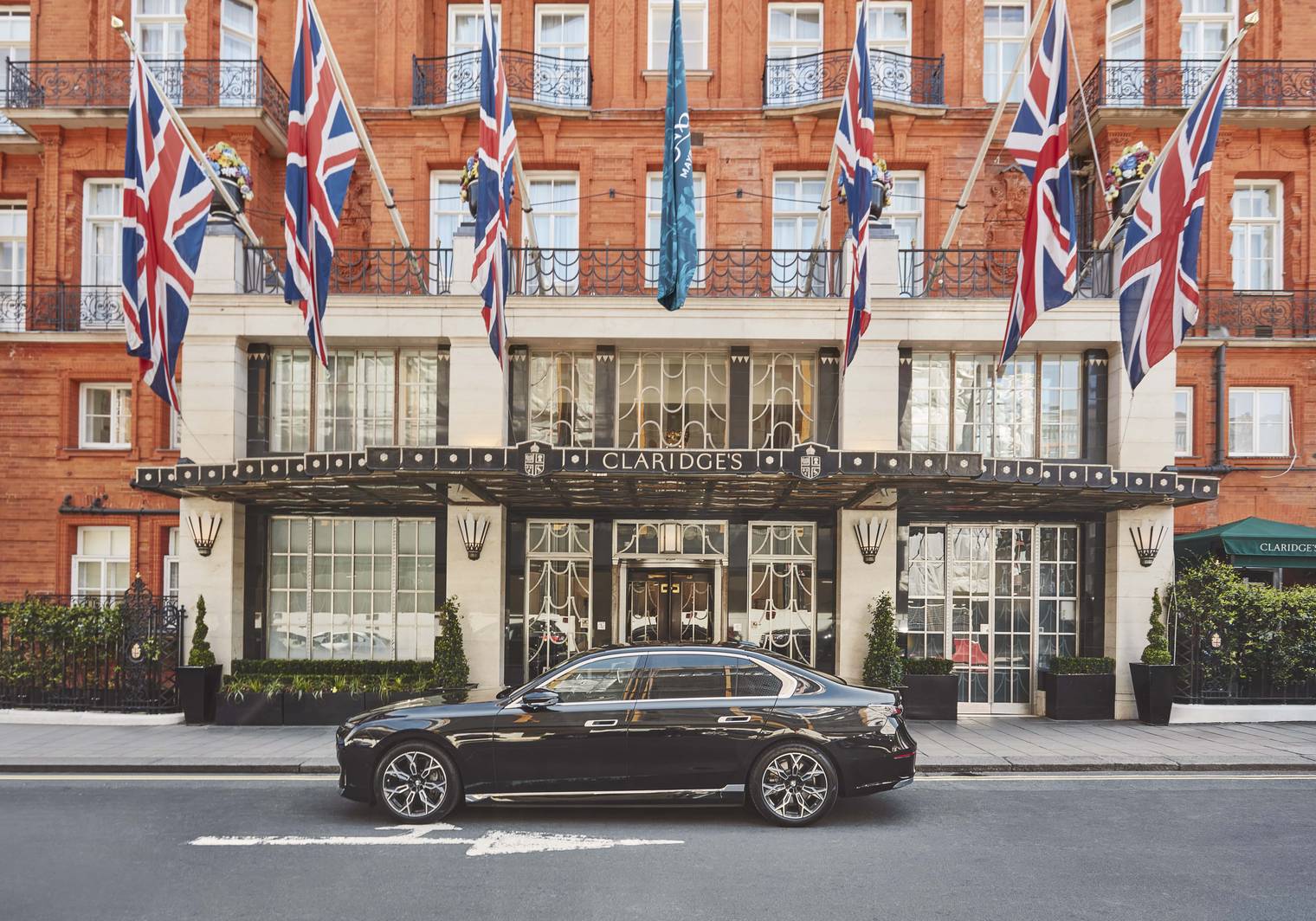 The grand entrance of Claridge's, adorned with Union Jack flags and a sleek black car parked outside.
