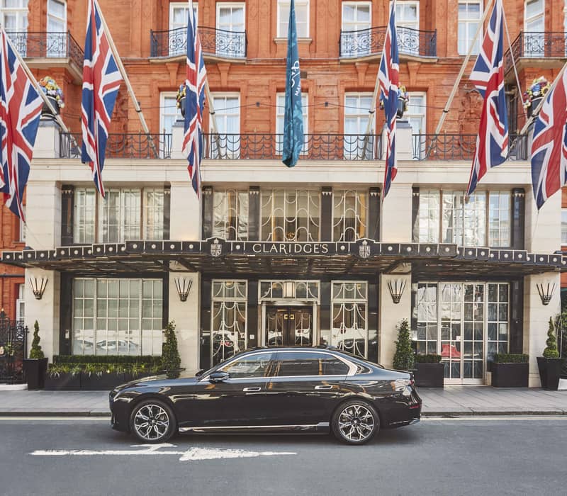 The grand entrance of Claridge's, adorned with Union Jack flags and a sleek black car parked outside.