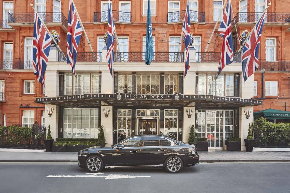 The grand entrance of Claridge's, adorned with Union Jack flags and a sleek black car parked outside.