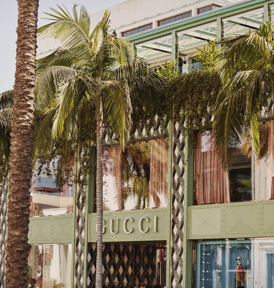 Gucci storefront on Rodeo Drive with palm trees, green lattice façade, and lush greenery under bright California sun.