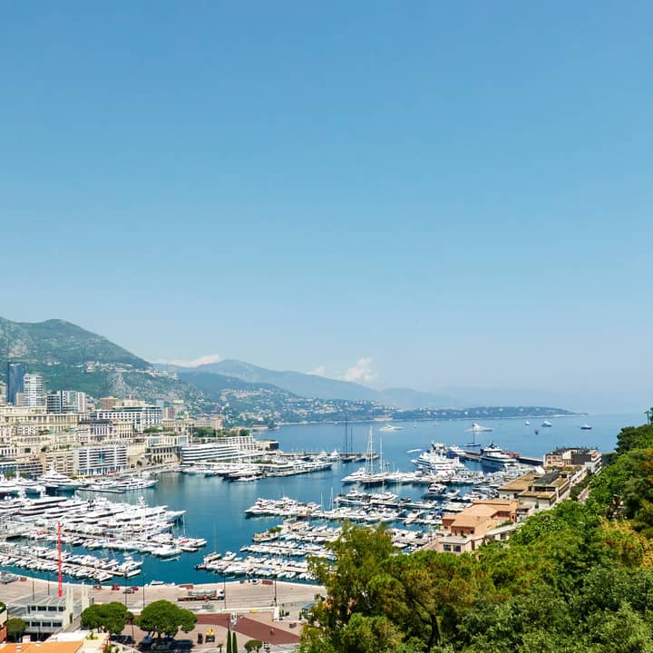 Panoramic view of Monte Carlo's marina with luxurious yachts, surrounded by hills and iconic architecture under a clear sky.