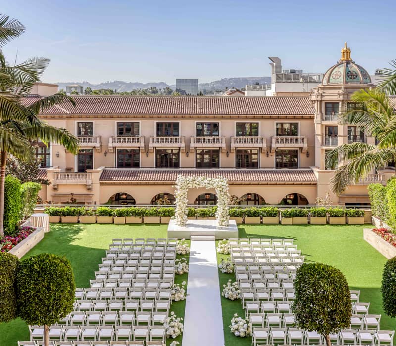 Outdoor luxury wedding ceremony setup with white chairs, floral arch, and lush greenery at an elegant Mediterranean-style venue.
