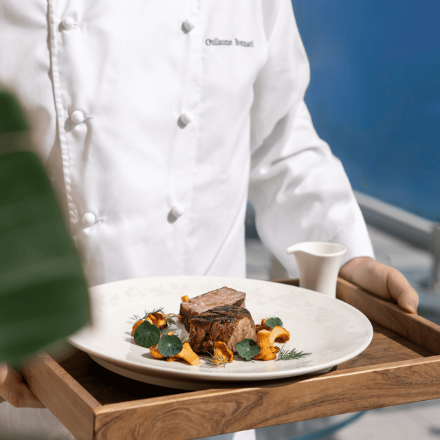 Chef presenting a gourmet dish of grilled meat with chanterelle mushrooms and herbs, elegantly served on a wooden tray.