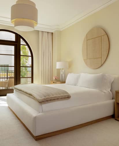 Serene, sunlit bedroom with neutral tones, arched window, minimalist furnishings, and soft textures in a modern design.