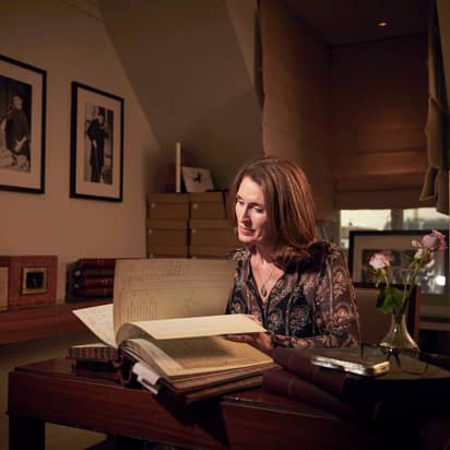 An archivist engrossed in historic documents, surrounded by books, framed photos, and a serene, softly lit study.