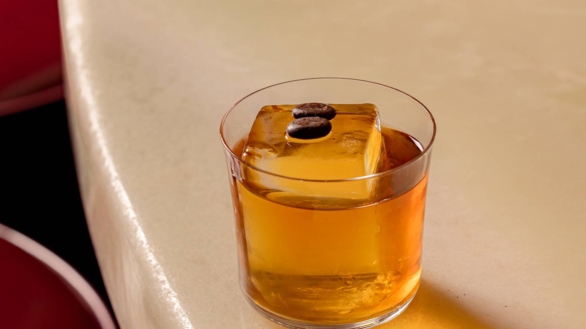 Classic whiskey cocktail with a large ice cube, resting on a sleek marble bar.