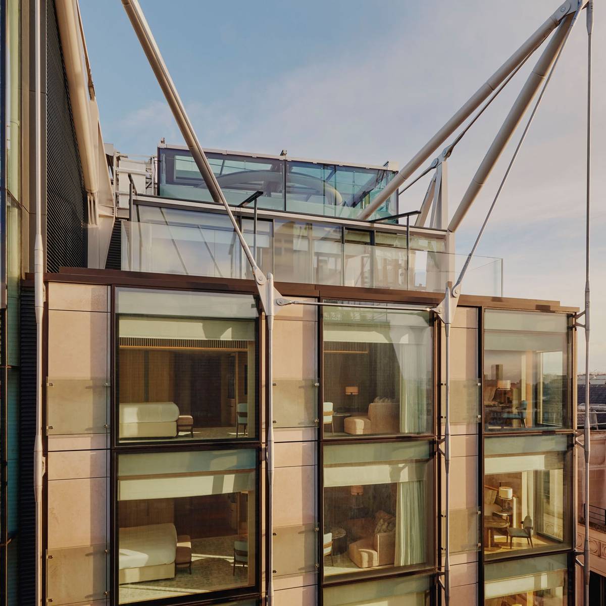 Exterior of The Emory, showcasing modern glass facade, elegant interiors, and striking architectural supports under a clear blue sky