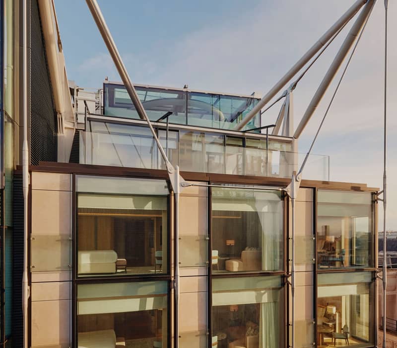 Exterior of The Emory, showcasing modern glass facade, elegant interiors, and striking architectural supports under a clear blue sky