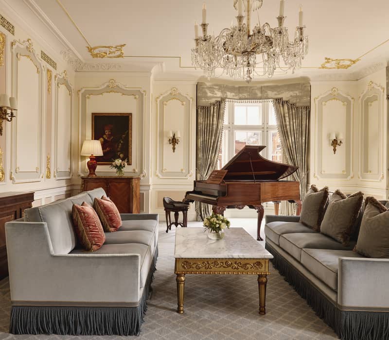 Spacious lounge with a sweeping curved staircase, modern fireplace, sculptural furniture, and floor-to-ceiling windows offering city views and natural light.