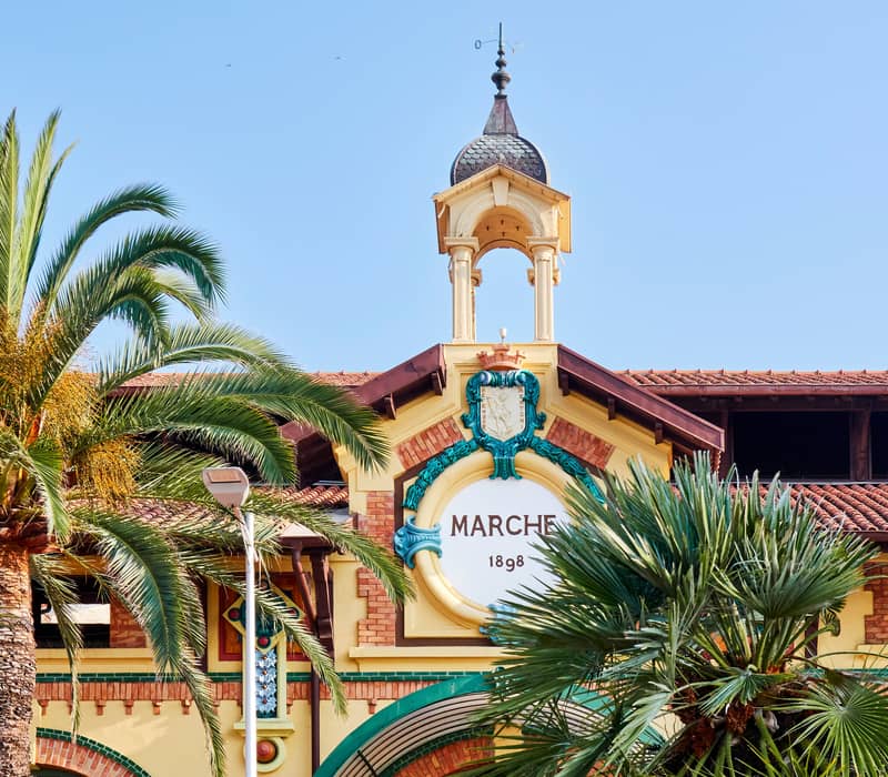 A historic market building adorned with intricate details, palm trees, and a decorative turret against a clear blue sky.