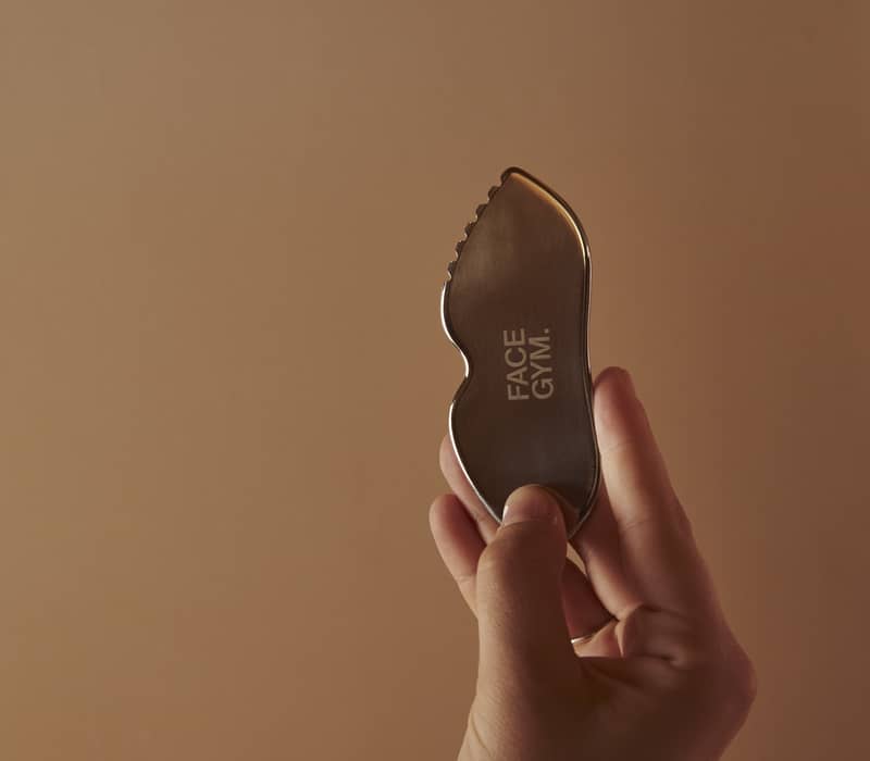 A sleek Face Gym tool, elegantly held up against a minimalist background, showcases refined craftsmanship and modern beauty innovation.