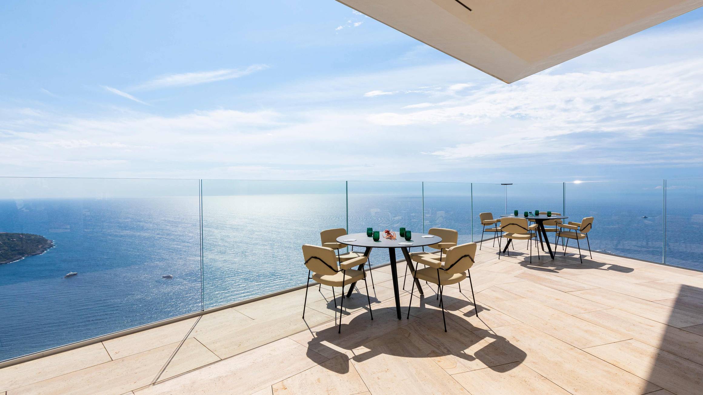 A breathtaking terrace with minimalist furnishings, glass railings, and panoramic views of the endless blue sea and sky.