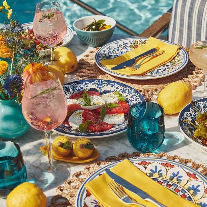 Colourful Italian-style meal and drinks by a poolside table, decorated with lemons and floral arrangements.