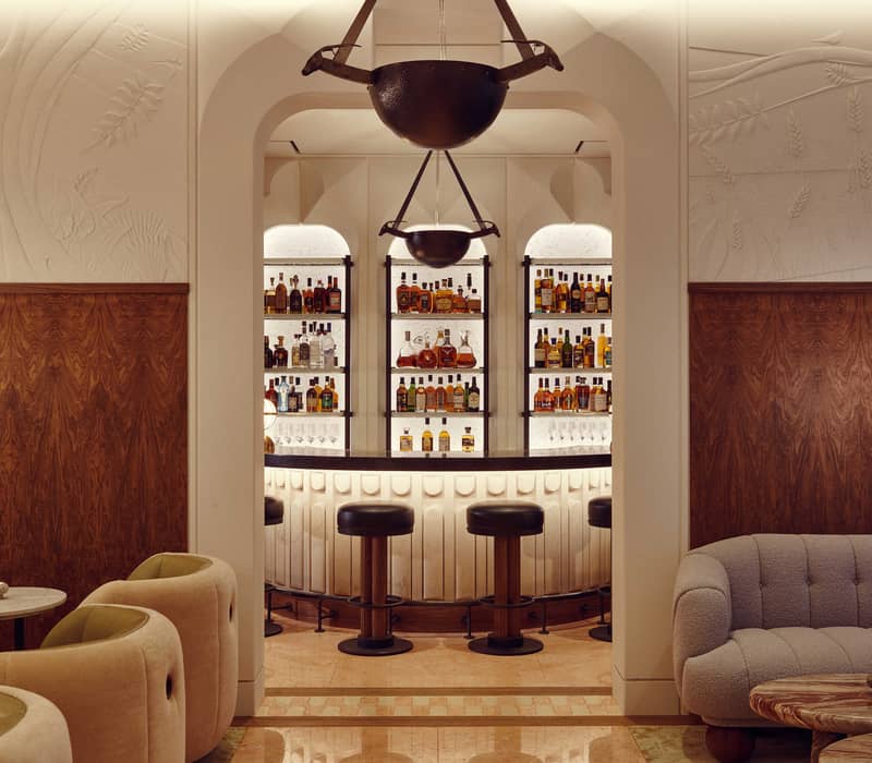 Elegant bar interior with plush seating, warm wood accents, and a backlit display of premium spirits under soft lighting.