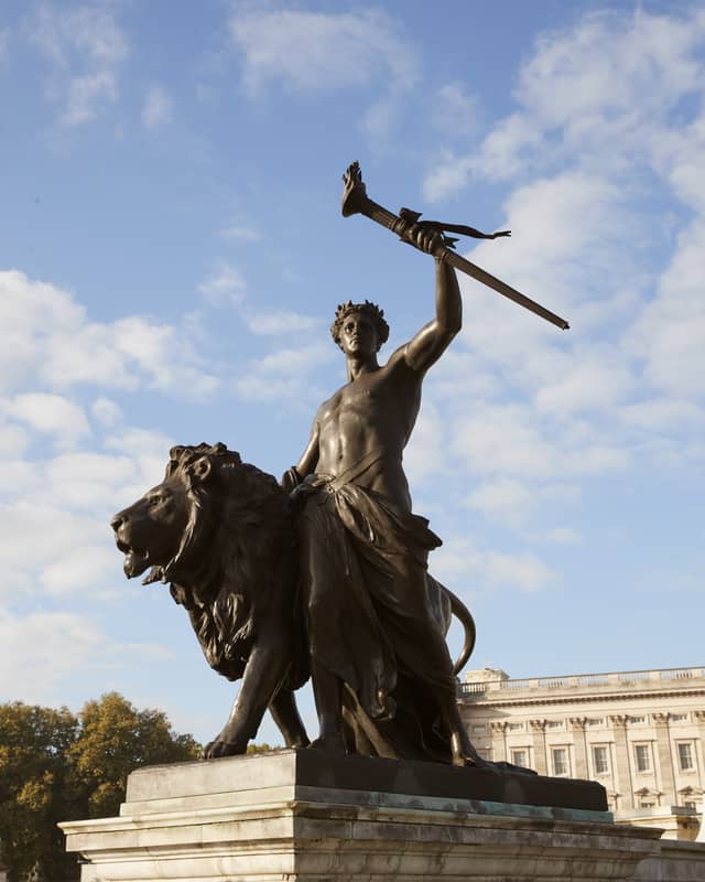 Powerful bronze statue of a lion and a warrior holding a torch, symbolizing strength and victory under a bright sky.
