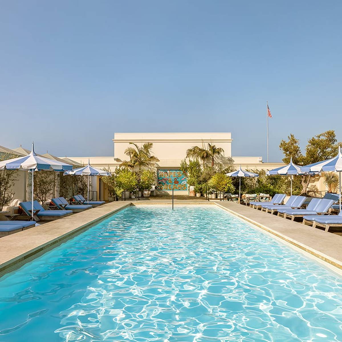 A serene rooftop pool with blue loungers, striped umbrellas, and lush greenery, exuding luxury under a clear sky.