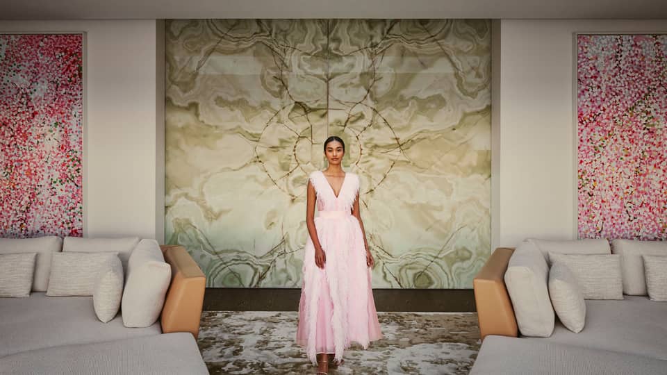 Elegant woman in a pink gown stands in a luxurious, art-filled living space with marble and contemporary furnishings.