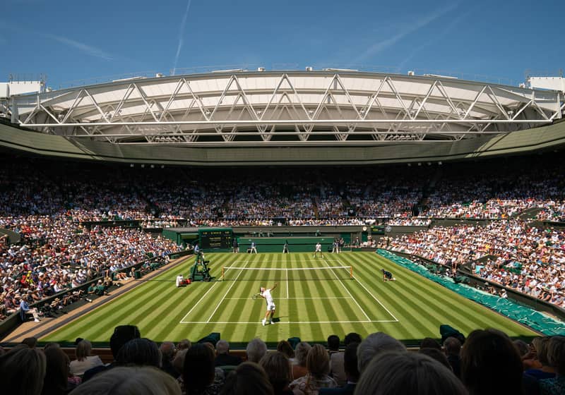 A thrilling grass-court tennis match unfolds under the iconic retractable roof of Wimbledon’s Centre Court.