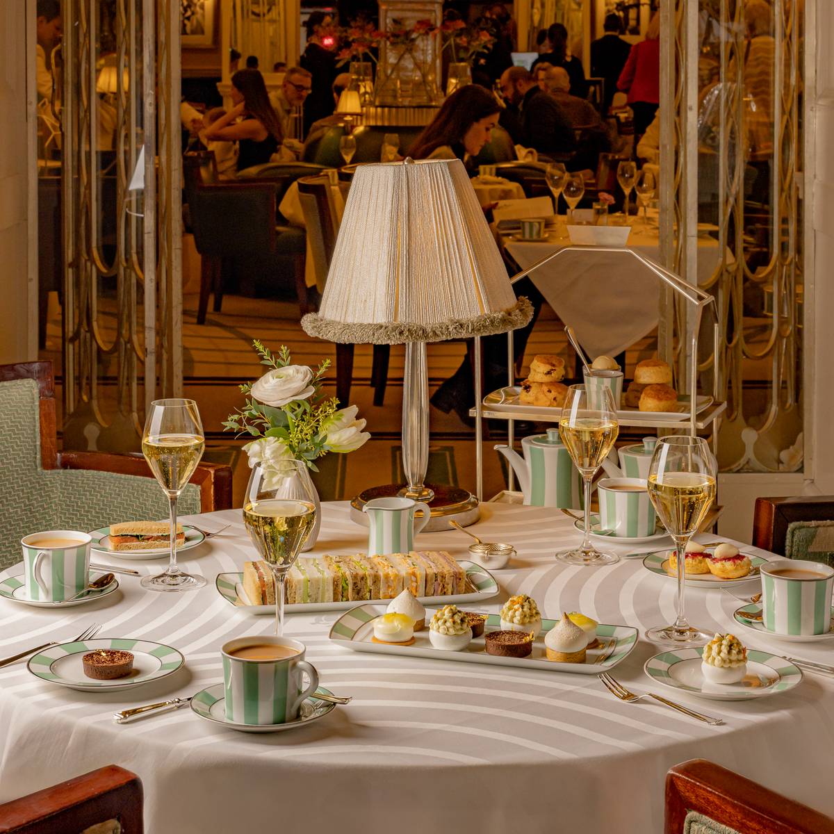 Elegant afternoon tea setting with fine china, champagne, and delicate pastries in a luxurious, warmly lit dining room.