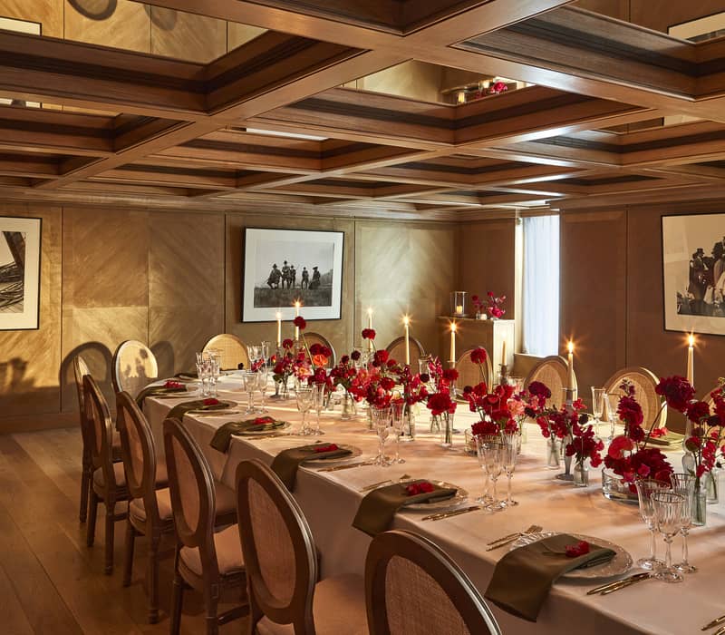 Luxurious dining room with a long table adorned with red floral arrangements, candlelight, and a mirrored ceiling reflecting elegance.