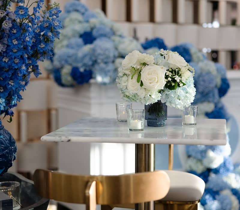 Elegant table setup with white roses, blue hydrangeas, and gold-accented chairs, creating a refined and celebratory ambiance.