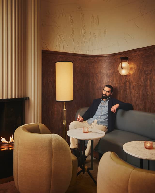A gentleman savours a quiet moment with a drink in a warmly lit, elegantly designed lounge featuring rich textures and soft lighting.