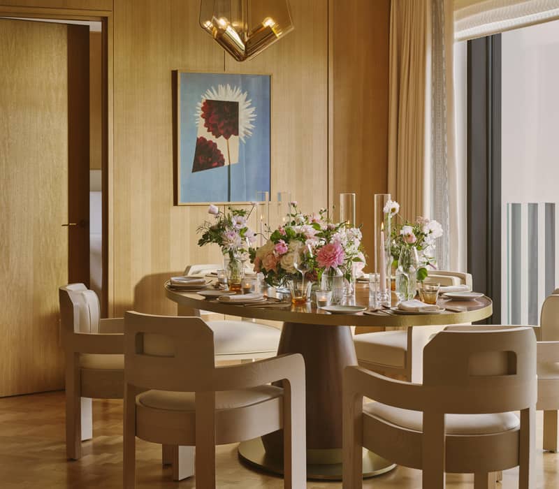 An elegant dining area featuring a round table with floral arrangements, modern chairs, warm wood accents, and natural light.