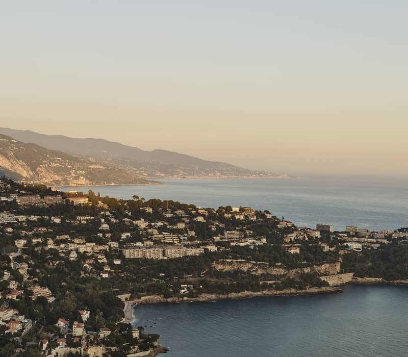 Aerial view of the French Riviera coastline at sunset, with hillside villas, lush greenery, and the Mediterranean Sea.