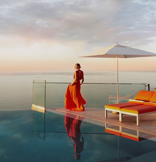 Woman at The Maybourne Riviera pool wearing an orange dress and looking at the view