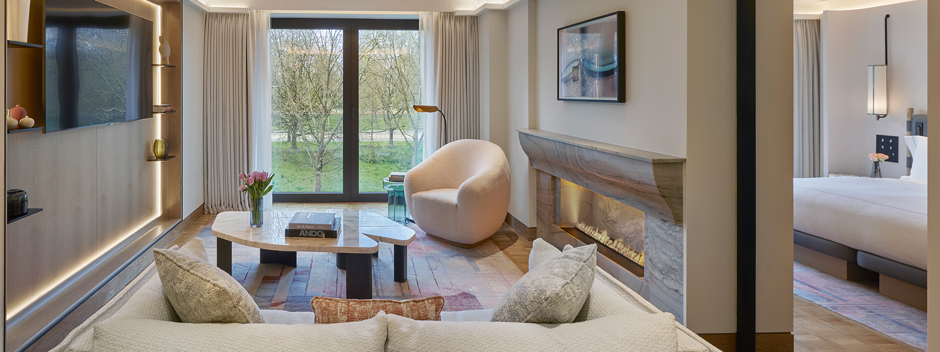Park Suite at The Berkeley - View of the lounge with sofa, armchair and coffee table, with tv on the left side and bedroom on the right side and window with view onto Hyde Park in the background.