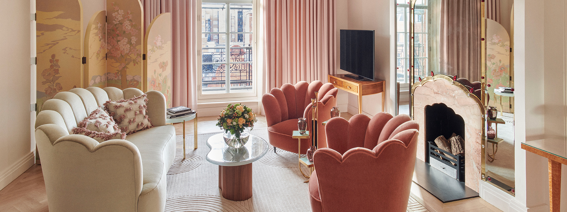 Mayfair Suite at Claridge's interior. Two pink scalloped arm chairs are in view to the left, to the right is a cream couch. Window in the background.