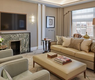 Linley interiors at Claridge's. Claridge's Suite view of the lounge with couch, coffee table and armchairs. TV and windows in the background.