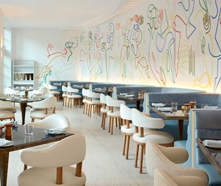 The Terrace at The Maybourne Beverly Hills - view of the room with tables and chairs next to the wall with colourful artwork on the wall.