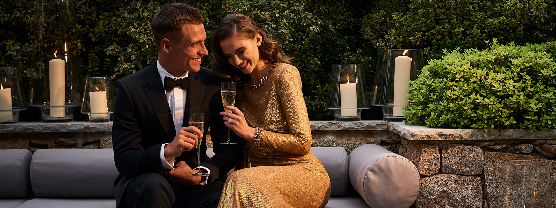Social occasions at The Berkeley. This image shows a man and woman in formal wear sitting down outside. They are next to each other and smiling, both are holding a glass of Champagne.