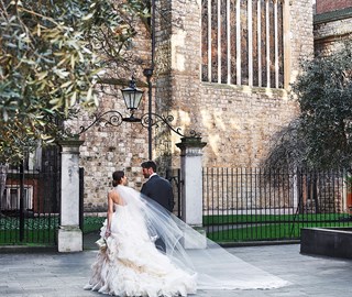 Weddings at The Connaught. This image shows a man and woman on their wedding day. They are looking at each other, behind them is a church and garden.