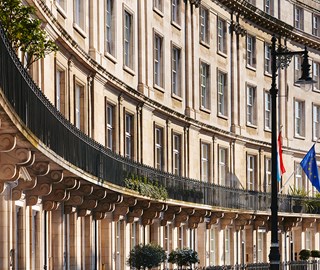 Round building façade in London, with a balcony on the first floor that has plants and flags on it.